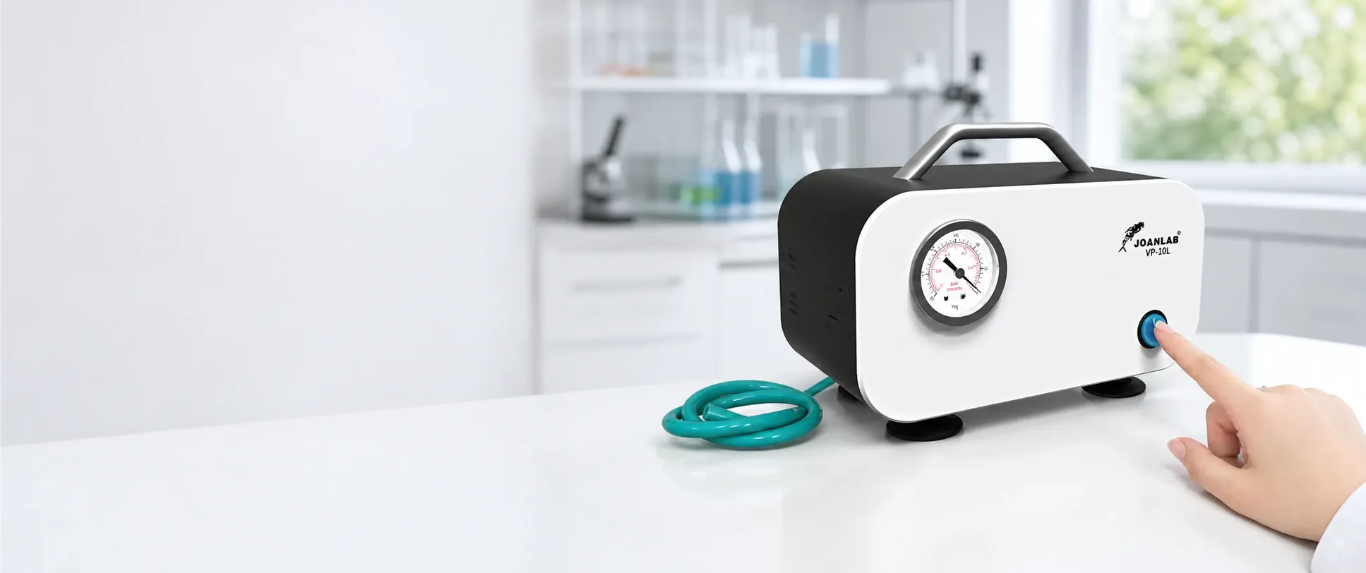 Compact benchtop laboratory vacuum pump with pressure gauge and carry handle on a clean lab bench, shown in use with a hand pressing the power button.